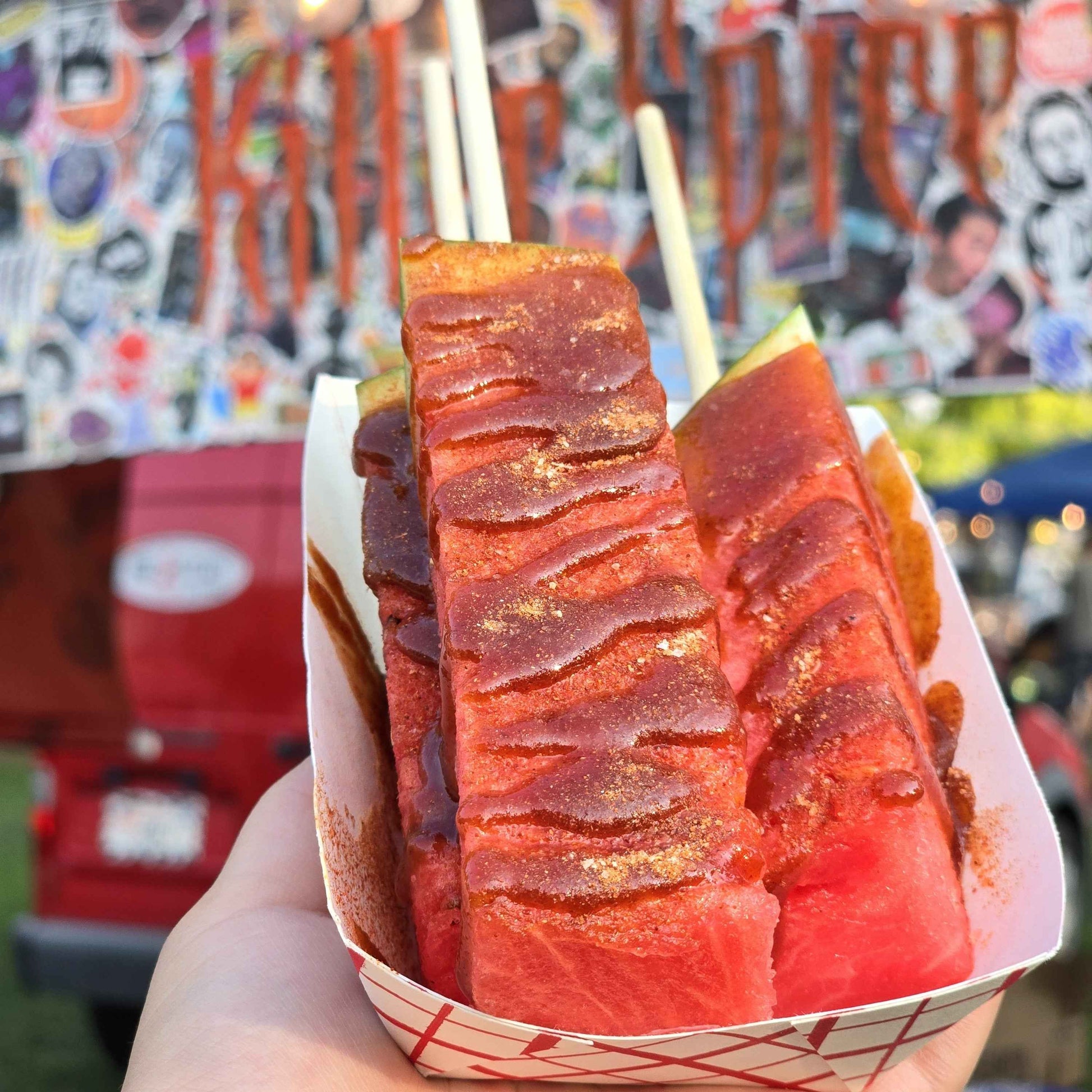 Fresh watermelon slices dusted with Killer Tamoy chamoy seasoning in a paper basket, showing vibrant red spice coating