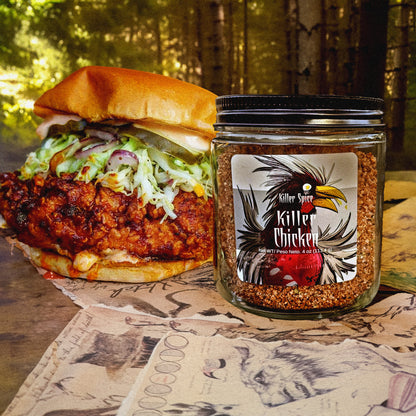 A jar of Killer Spice's Killer Chicken Sweet and Savory Rub next to a spicy chicken sandwich on a table with a woodland backdrop.