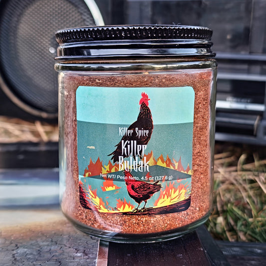 A jar of "Killer Buldak" from Killer Spice on a straw surface with a graphic of a rooster and flames on the label.