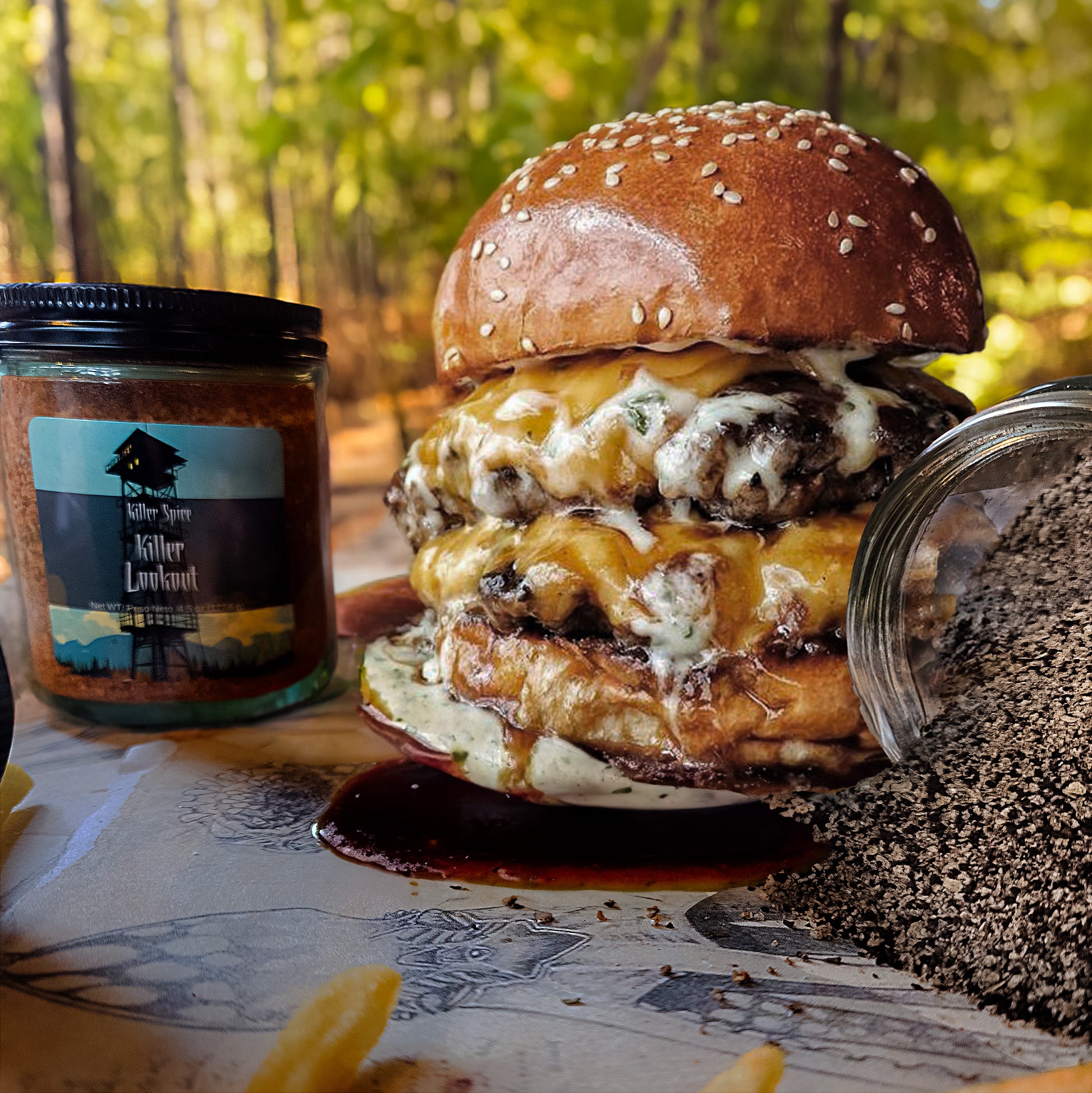 A double cheeseburger with a side of fries, paired with a jar of sauce and a spilled pile of Killer Lookout (Cajun Spice) on a wooden surface, with a blurred forest backdrop.