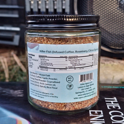 A jar of Killer Fish spice blend for seafood dishes, with ingredients like infused coffee, rosemary, and exotic spices on a wooden surface.