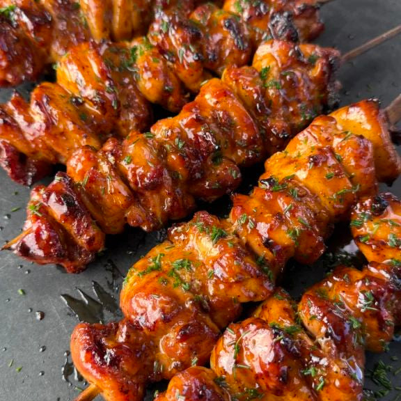 Skewers of grilled chicken with a glossy sauce on a dark surface