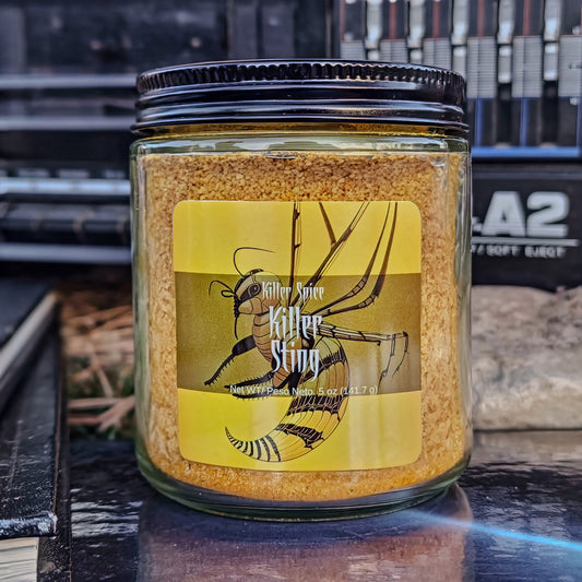 A jar of Killer Spice's Killer Sting honey, habanero spice blend dry rub on a shelf with a black lid and yellow label.