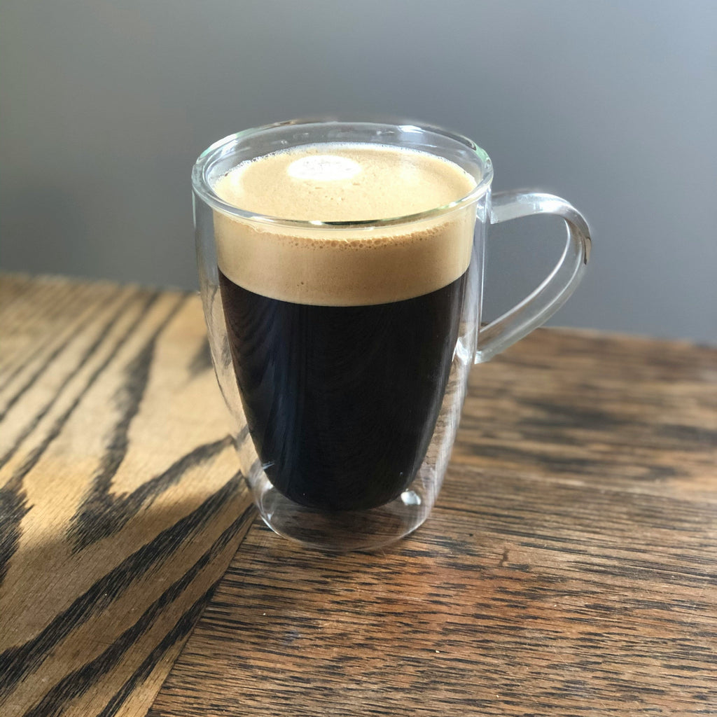 Glass mug with a layered coffee drink on a wooden surface