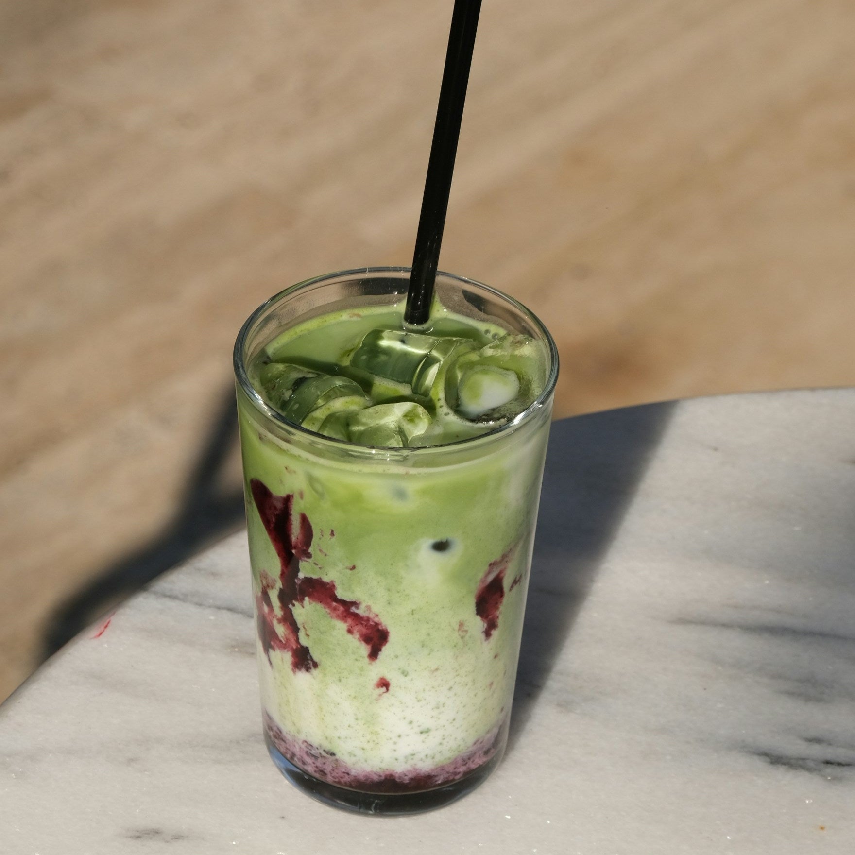 Green smoothie in a glass with a straw on a marble surface