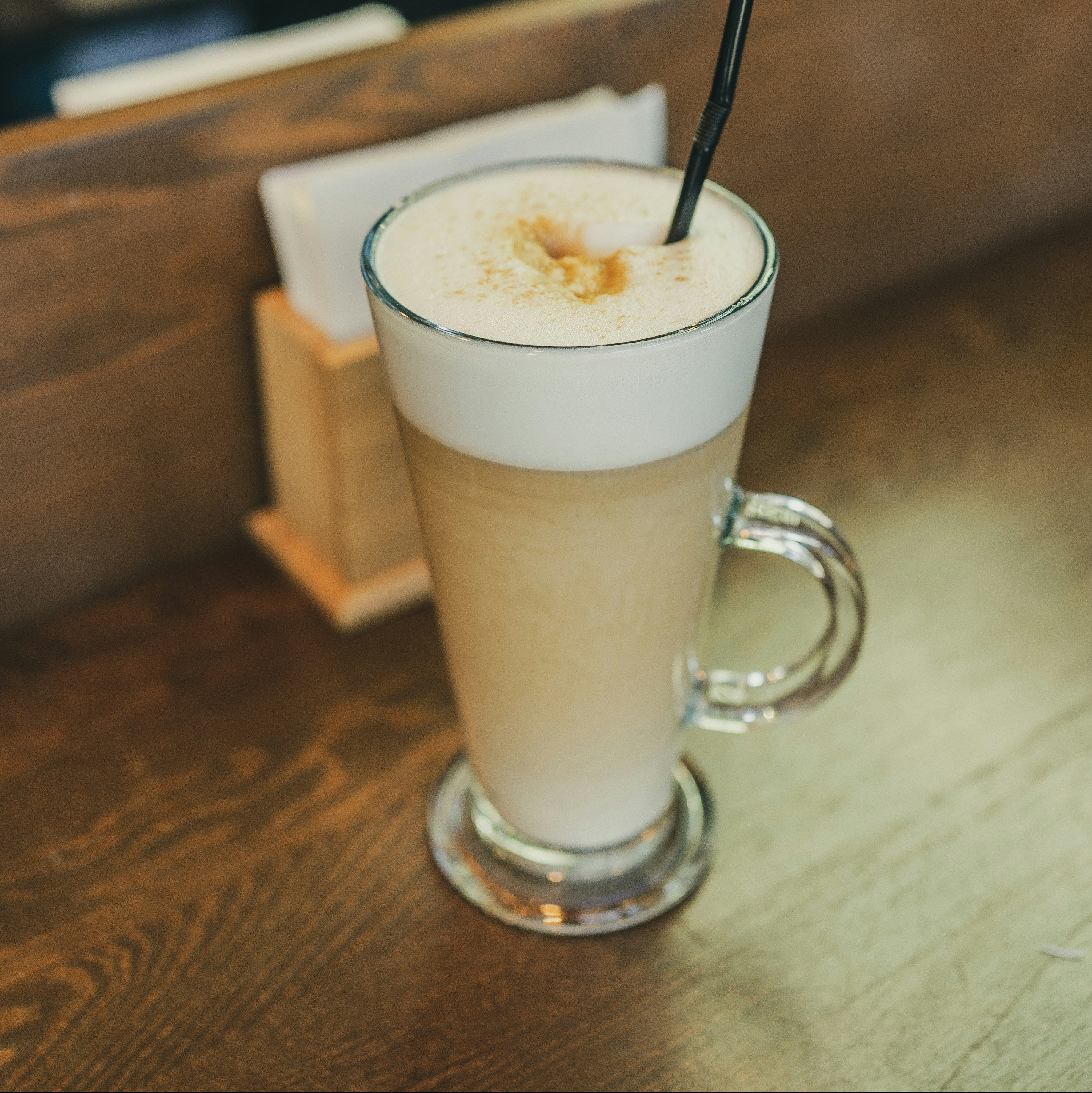 Glass of latte with a black straw on a wooden table