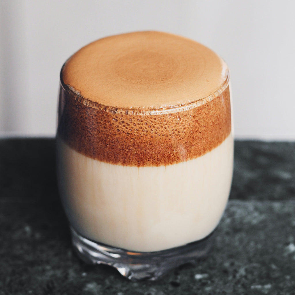 Glass of dalgona coffee with a brown foam layer on a dark surface.