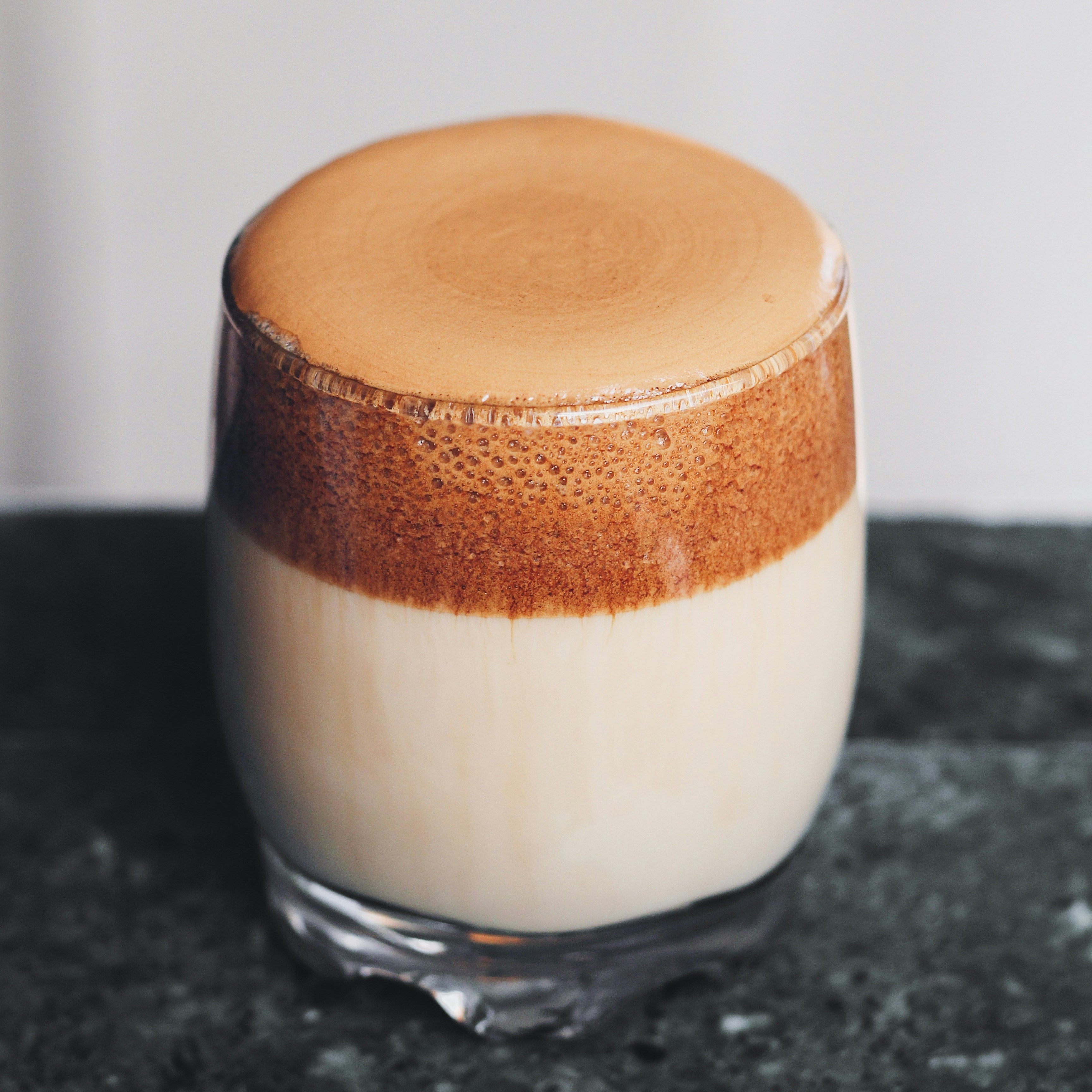 Glass of dalgona coffee with a brown foam layer on a dark surface.