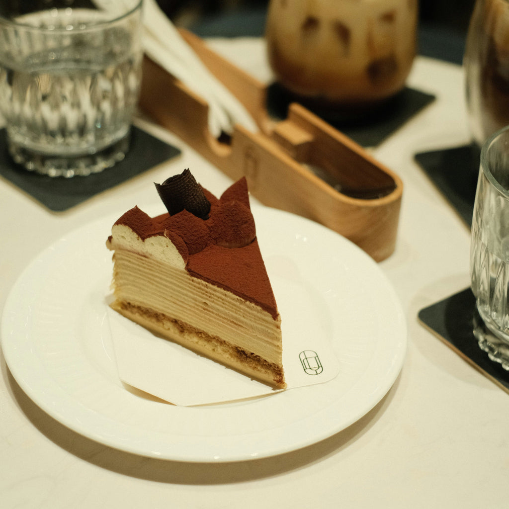 Slice of layered cake on a white plate with drinks in the background