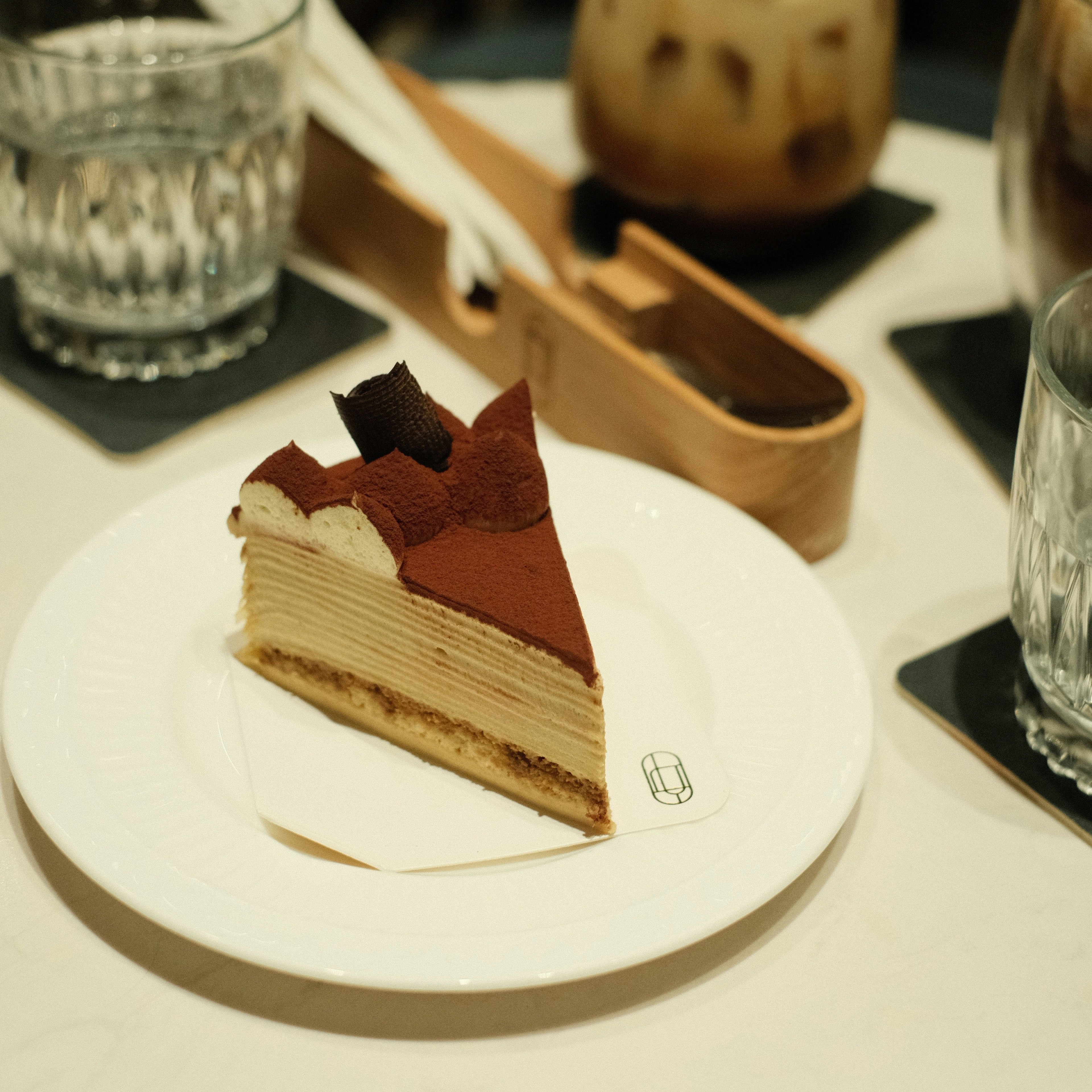 Slice of layered cake on a white plate with drinks in the background