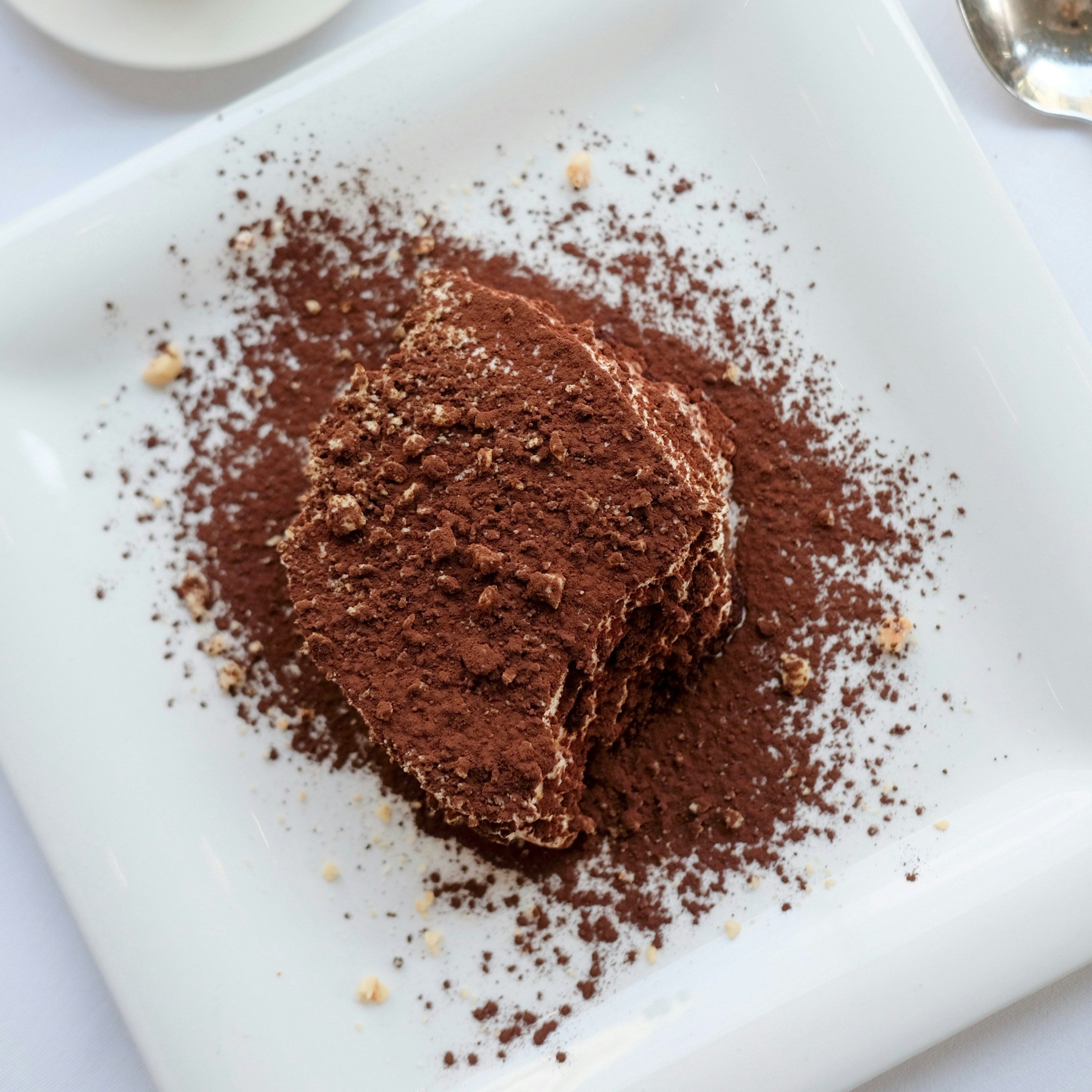 Chocolate cake with cocoa powder on a white plate next to a cup of coffee.