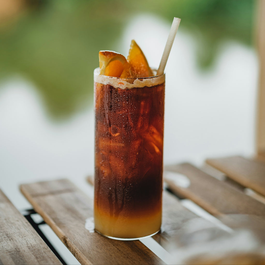 Cold brew coffee with ice and a straw on a wooden table outdoors.