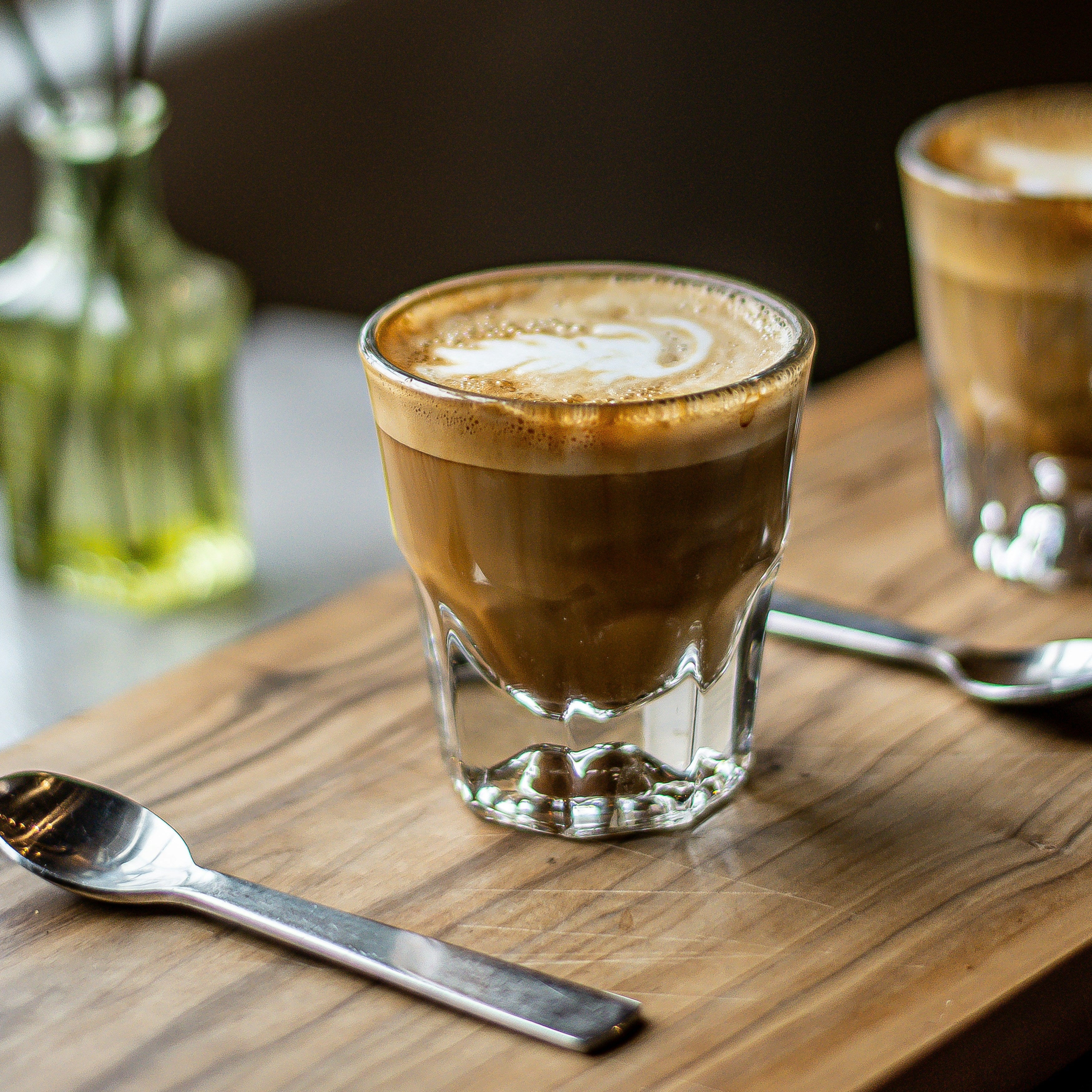 Two glasses of coffee on a wooden table with a blurred background