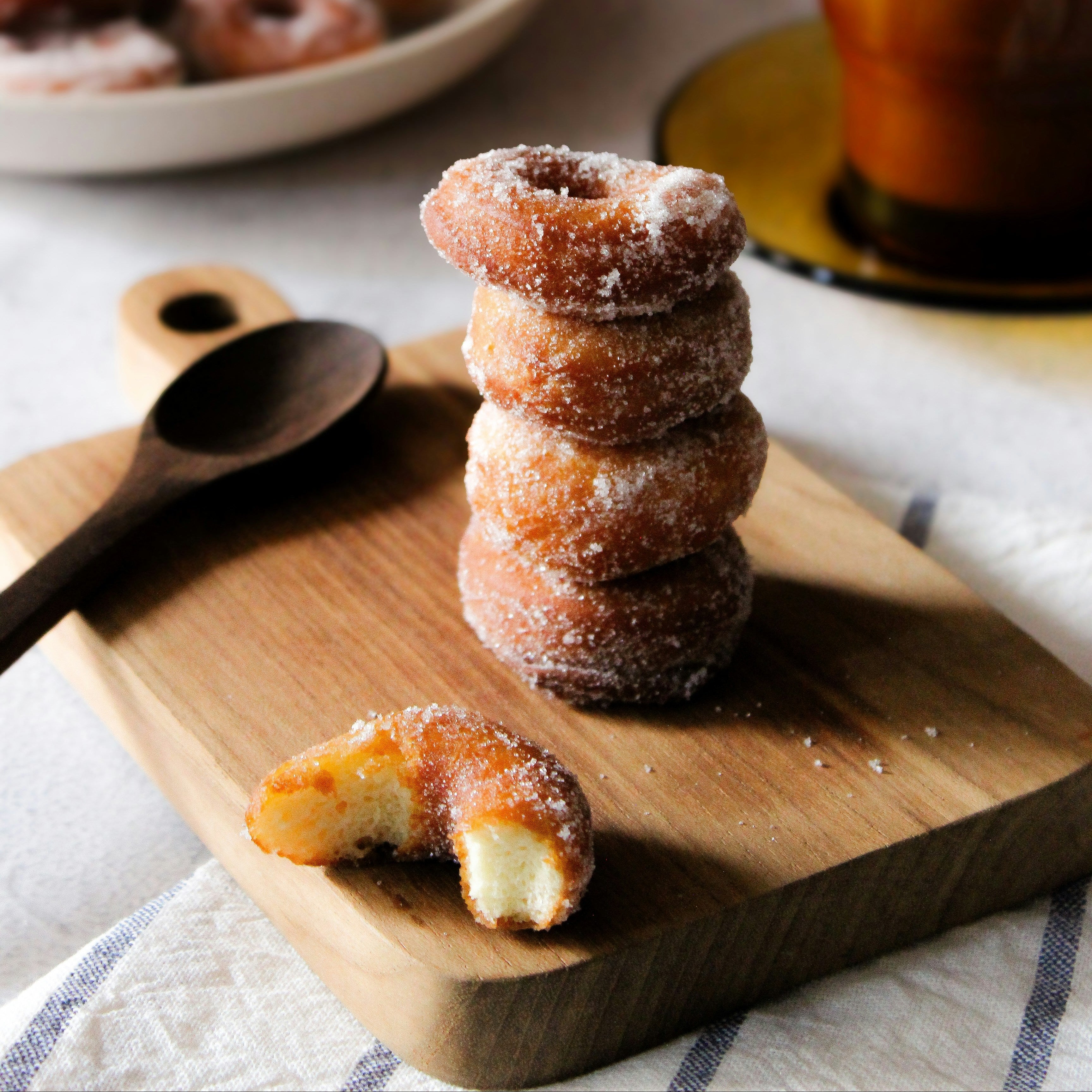 Stack of sugared donuts on a wooden cutting board with a cup of coffee in the background.