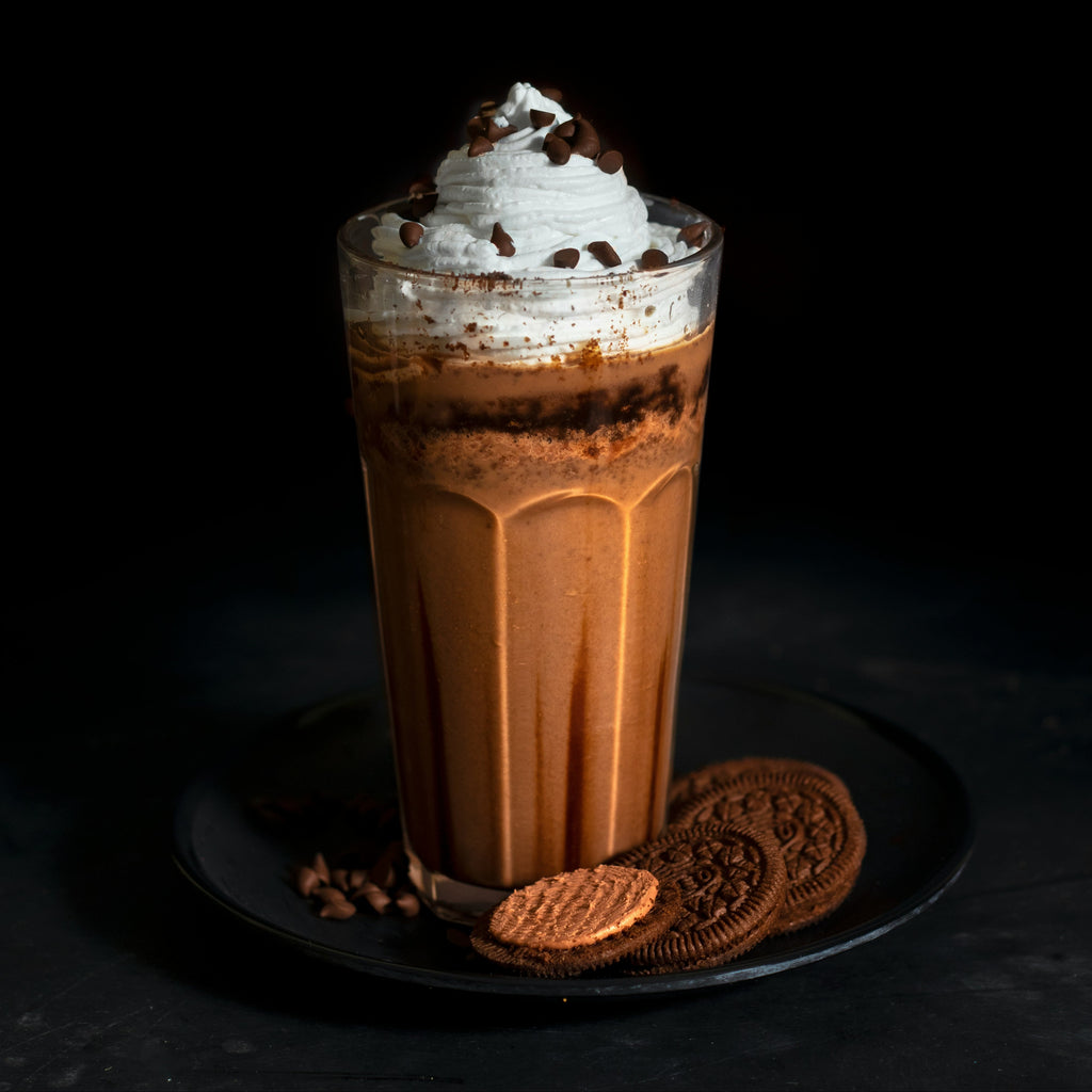 Glass of iced coffee with whipped cream and cookies on a dark background