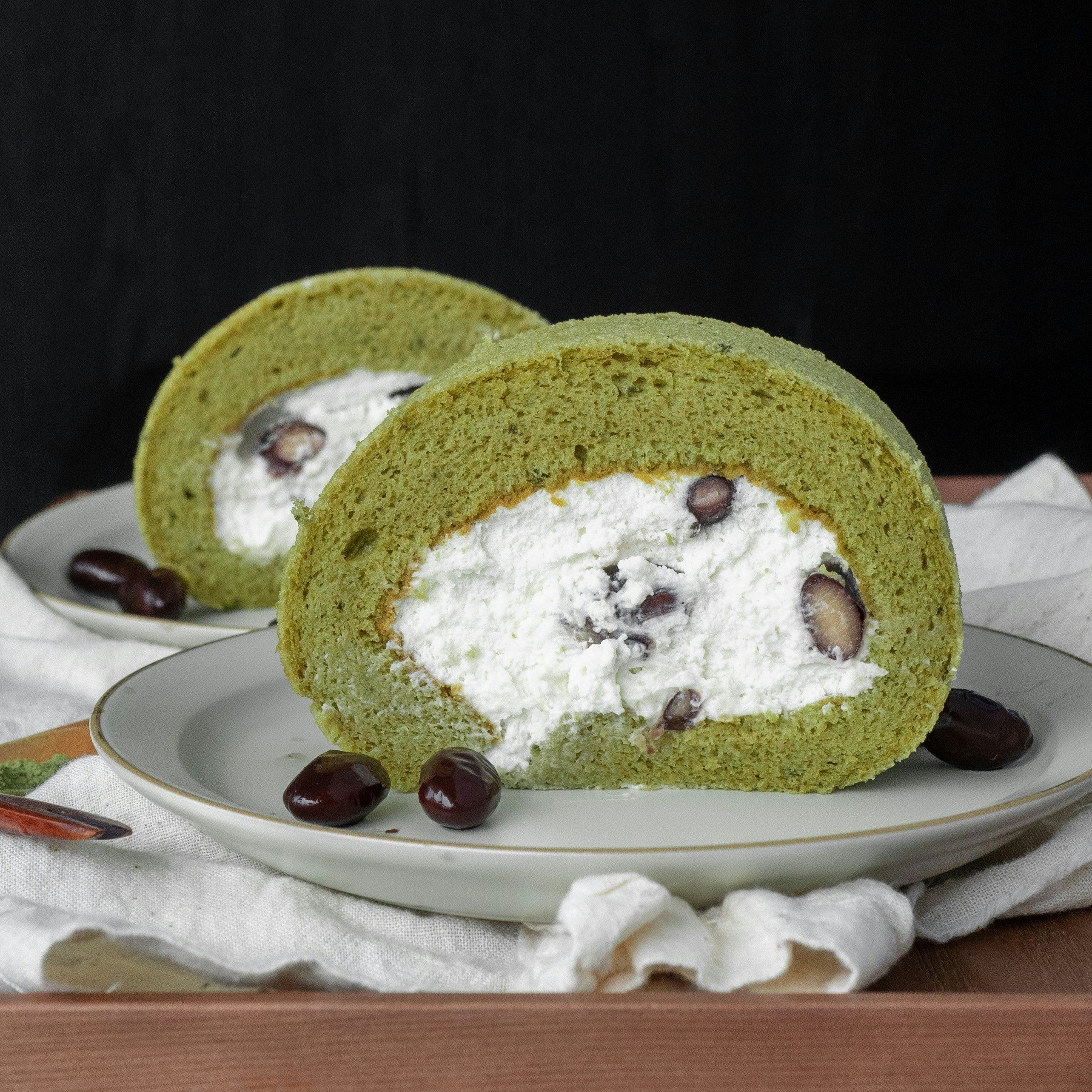Green matcha roll cake with white filling and chocolate chips on a plate.